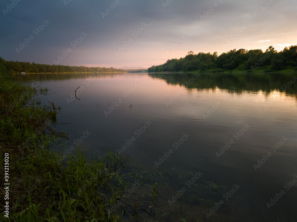 The beautiful landscape of the Sava River during a gloomy evening with a sunny pink glow that stretches under the clouds, and the mountains in the mist. The beautiful landscape of the Sava River during a gloomy evening with a sunny pink glow that stretches under the clouds, and the mountains in the mist.