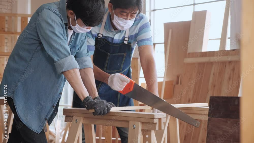 Asian man carpenter training showing apprentice how to use hand sawing in the workshop. Asian man carpenter training showing apprentice how to use hand sawing in the workshop.