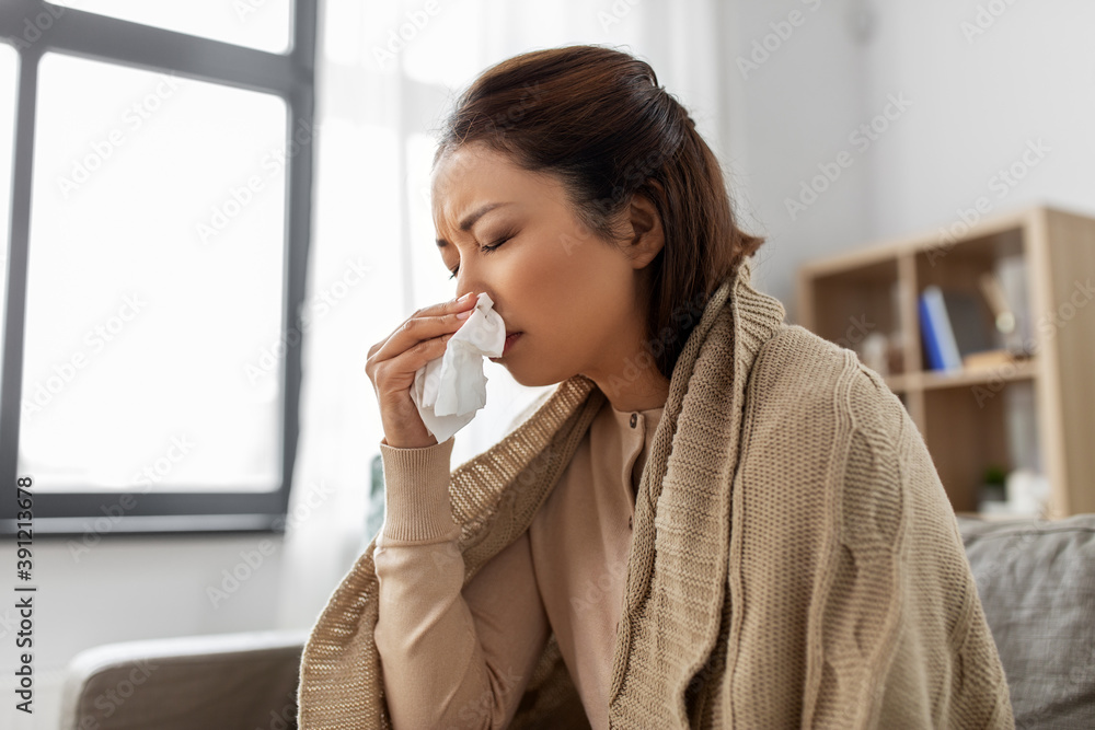 healthcare, cold and people concept - sick asian woman in blanket taking paper tissue from box and blowing her nose at home healthcare, cold and people concept - sick asian woman in blanket taking paper tissue from box and blowing her nose at home
