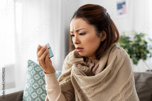 health, cold and people concept - sad sick young asian woman in blanket with medicine at home