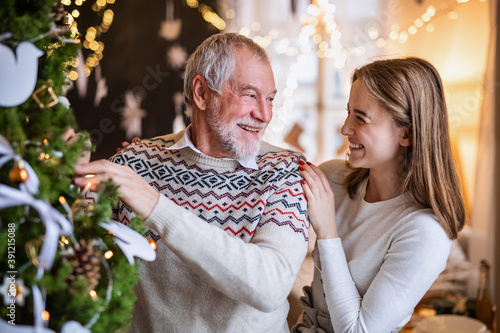 Young woman with senior grandfather indoors at home at Christmas, decorating tree.