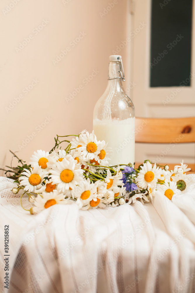 Simply stylish wooden kitchen with bottle of milk and glass on table, summer flowers camomile, healthy foog moring concept Simply stylish wooden kitchen with bottle of milk and glass on table, summer flowers camomile, healthy foog moring concept