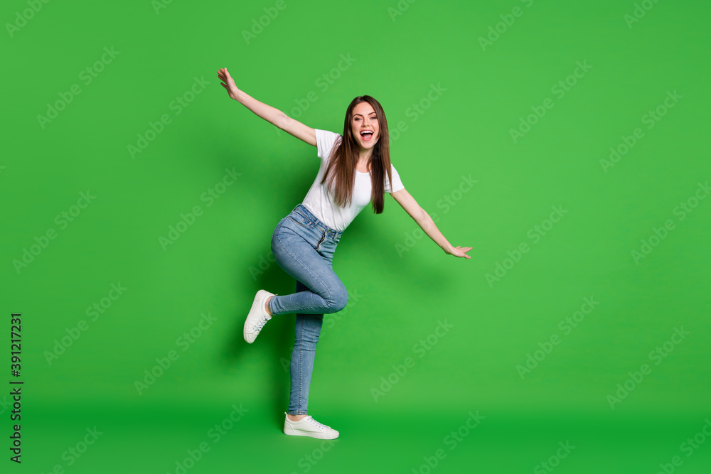 Full length photo of cute pretty dreamy lady raise hands funny plane dance wear jeans t-shirt footwear isolated green background Full length photo of cute pretty dreamy lady raise hands funny plane dance wear jeans t-shirt footwear isolated green background