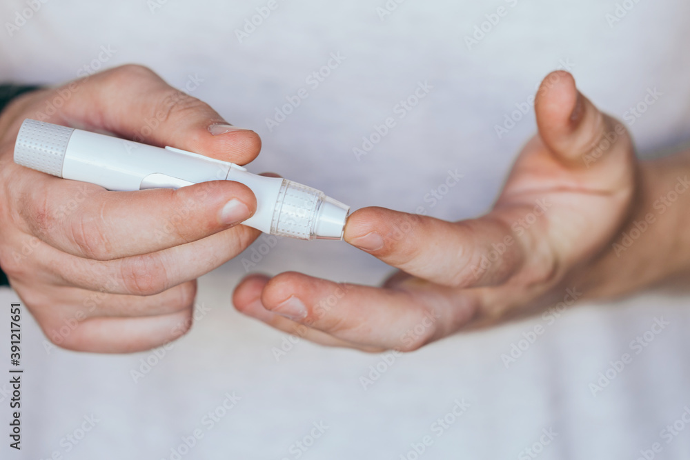 Close up of a man's hand using a lancet on his finger to check blood sugar using a glucose meter, using as medicine, diabetes, glycemia, healthcare and people concept.