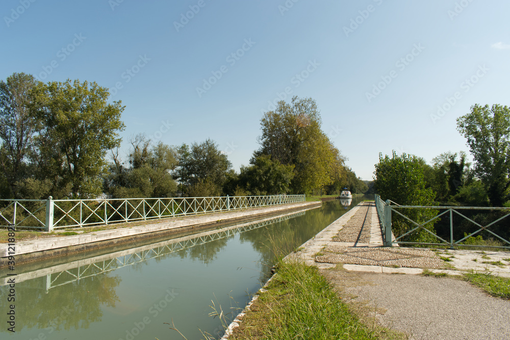 Obraz premium Un bateau de plaisance s'approche de ce pont canal qui lui permettra de passer sans encombre la rivière située en dessous sur le Canal Latéral à la Garonne