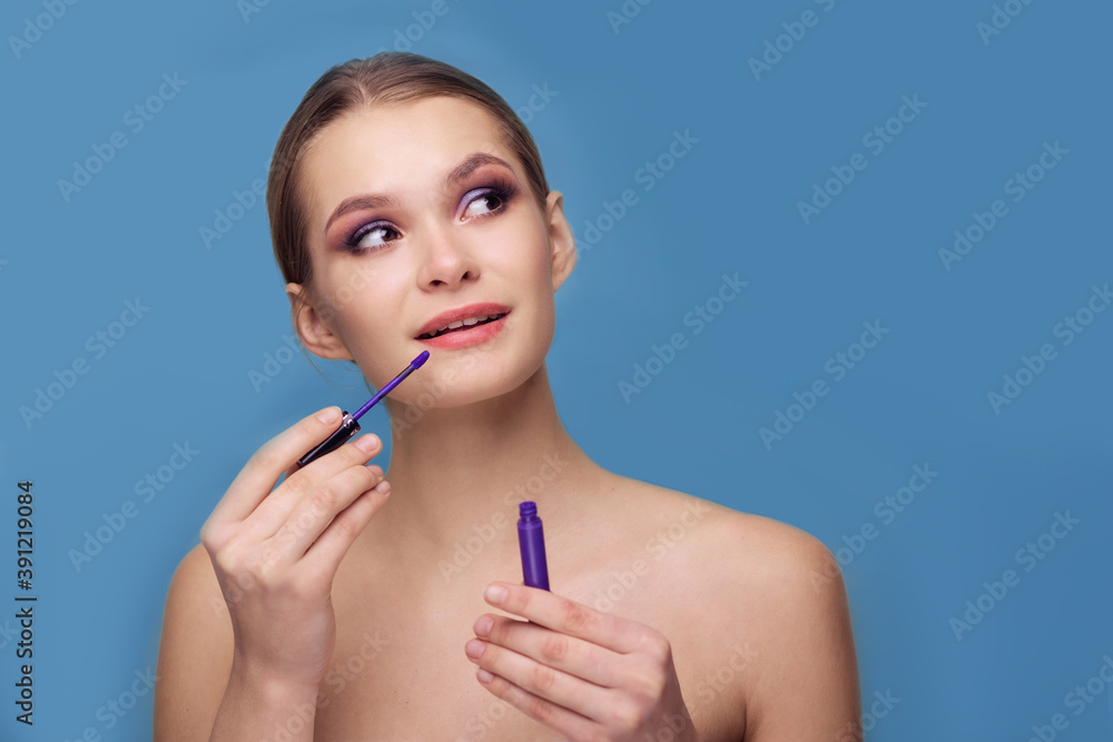 Beautiful young woman on a blue background with lipstick. Foolish mood. Evening colored smoky makeup. Purple lip gloss. Make up artist Visagiste. Youth. Cosmetics for young. Sensuality sexuality girl Beautiful young woman on a blue background with lipstick. Foolish mood. Evening colored smoky makeup. Purple lip gloss. Make up artist Visagiste. Youth. Cosmetics for young. Sensuality sexuality girl
