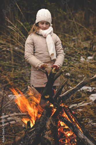 Teen girl warms his hands by the bonfire. Hiking in the forest concept. Late fall. Hiking in the forest concept. Late autumn. Vertical shot