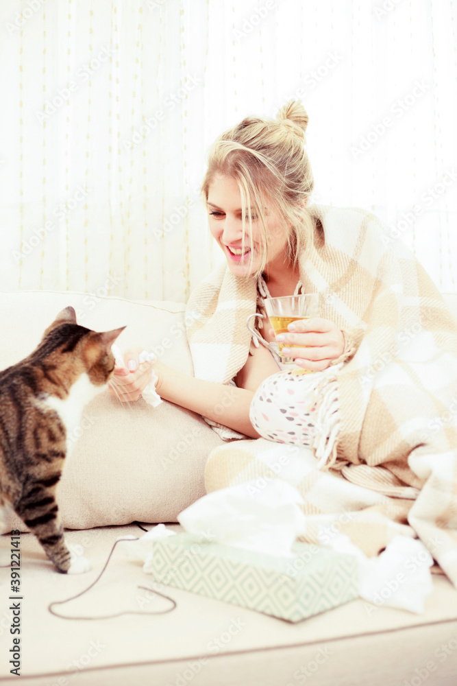 Sick, allergic young woman petting her cat while wrapped in a cozy blanket in living room Sick, allergic young woman petting her cat while wrapped in a cozy blanket in living room