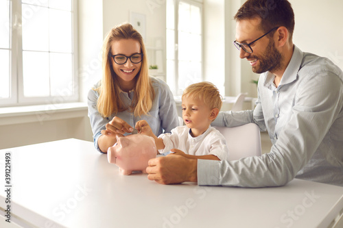 Foto Little boy with his parents puts coins in a piggy bank sitting at a table in the room