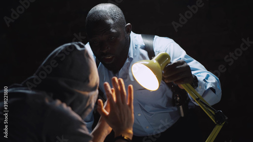 African officer interrogating man suspected of crime glowing light of lamp into face