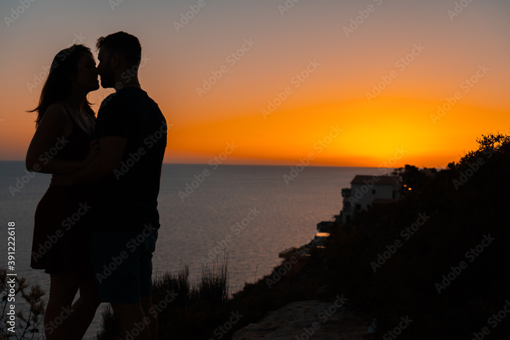 Young couple kiss each other at sunset from a cliff overlooking the sea