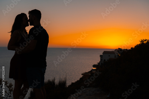 Young couple kiss each other at sunset from a cliff overlooking the sea