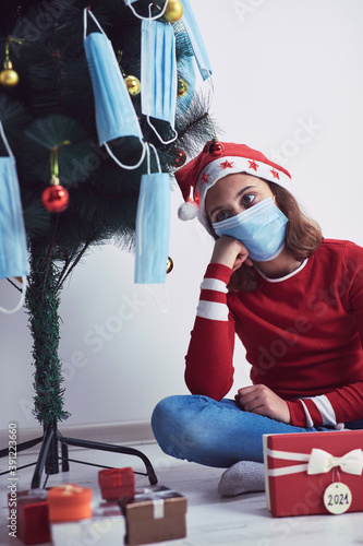 Small girl decorating christmas tree with medical masks during virus pandemic 2020 / 2021.