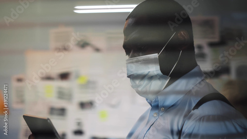 View through window of african police officer in protective mask using tablet pc at police department photo