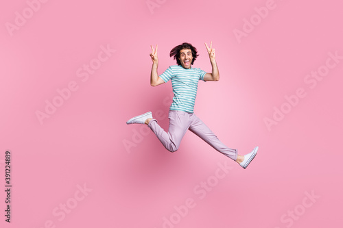 Full length photo of funny young guy dressed casual clothes jumping showing v-sign isolated color background © deagreez