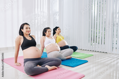 Happy pretty young Vietnamese pregnant women sitting on yoga mats in training class