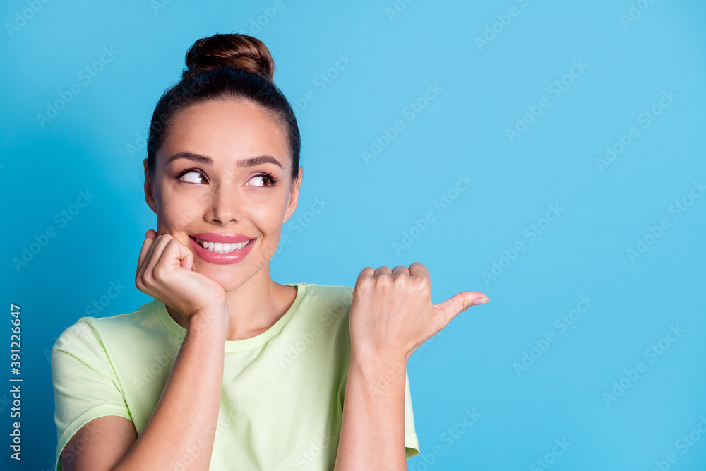 Photo of cheerful lady point thumb finger empty space isolated over blue pastel color background Photo of cheerful lady point thumb finger empty space isolated over blue pastel color background