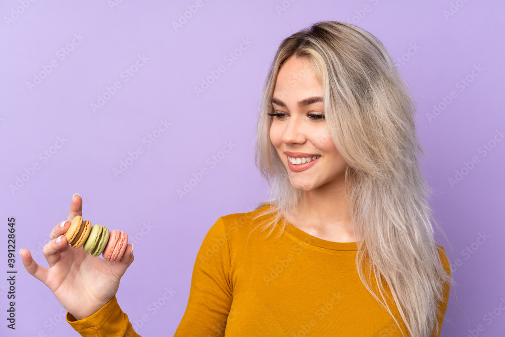Teenager girl over isolated purple background holding colorful French macarons and happy Teenager girl over isolated purple background holding colorful French macarons and happy