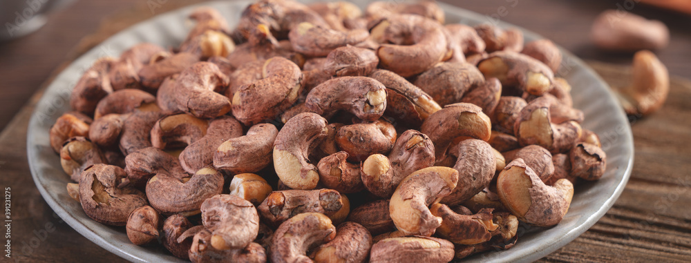Cashew nuts with peel in a plate on wooden tray. Cashew nuts with peel in a plate on wooden tray.