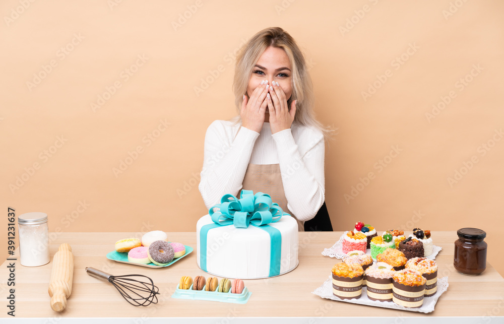 Teenager pastry chef with a big cake in a table with surprise facial expression