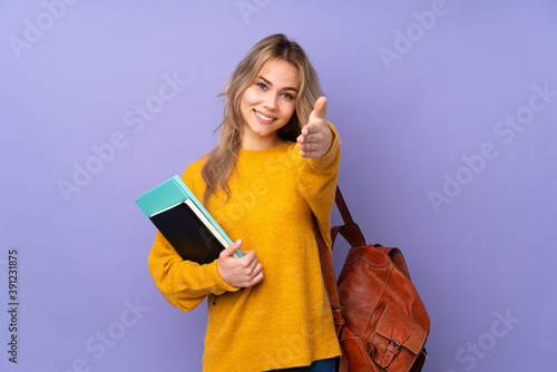 Teenager Russian student girl isolated on purple background shaking hands for closing a good deal