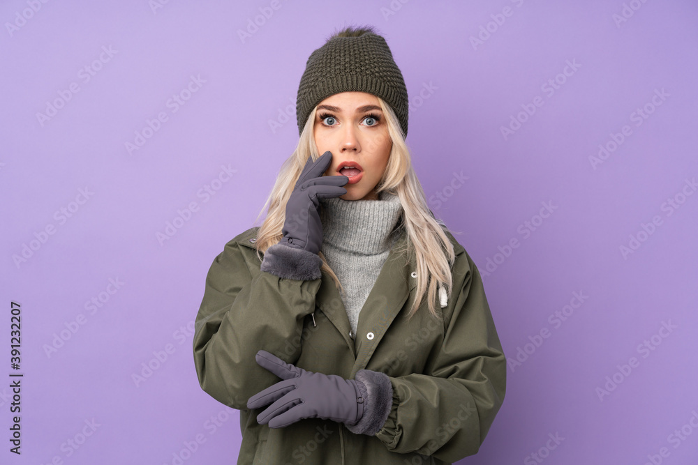 Teenager blonde girl with winter hat over isolated purple background surprised and shocked while looking right Teenager blonde girl with winter hat over isolated purple background surprised and shocked while looking right