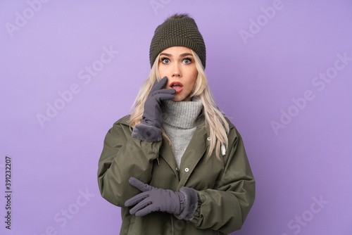 Teenager blonde girl with winter hat over isolated purple background surprised and shocked while looking right