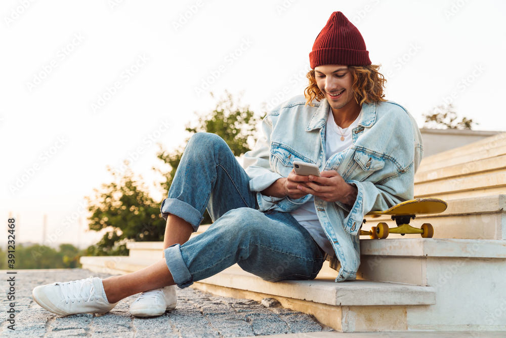 Positive young curly man scater using mobile phone