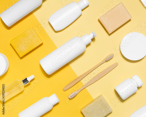 Cosmetic pattern on yellow background. Tubes with cream, glass bottle with oil, toothbrush, soap, dispensers and jars. Mock up for branding. Flat lay