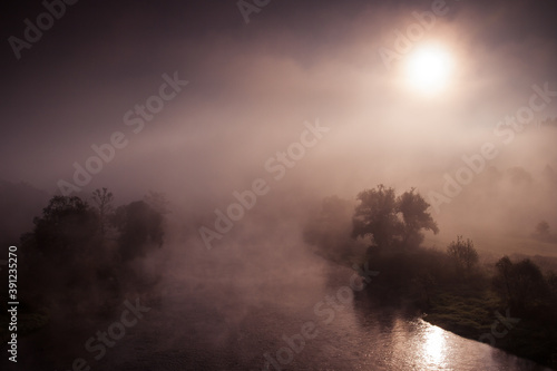 crazy foggy morning with hidden sun, autumn fog over the river with trees around
