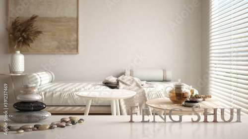 White table shelf with pebble balance and 3d letters making the word feng shui over white and wooden living room with sofa, tables with teapot and tea cup, zen concept interior design