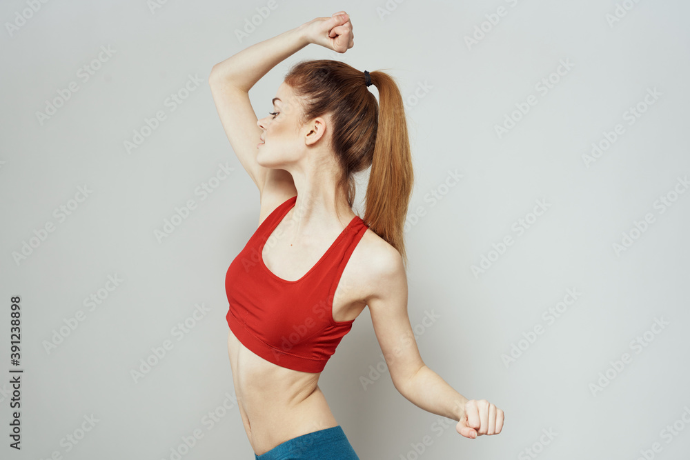 A woman in a red T-shirt on a light background is engaged in fitness gestures with her hands a slim figure A woman in a red T-shirt on a light background is engaged in fitness gestures with her hands a slim figure