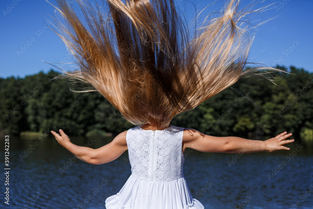 Naklejka premium A six year old girl is wearing a white dress. Beautiful long hair. Walk near the river on the background of the forest