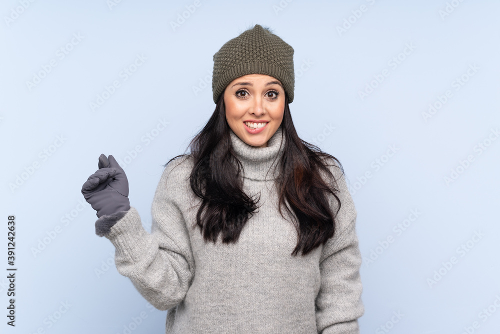 Young Colombian girl with winter hat over isolated blue background having doubts and with confuse face expression Young Colombian girl with winter hat over isolated blue background having doubts and with confuse face expression