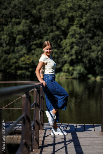 A beautiful girl of European appearance. A young woman is walking by the river. Dressed in jeans and a T-shirt.