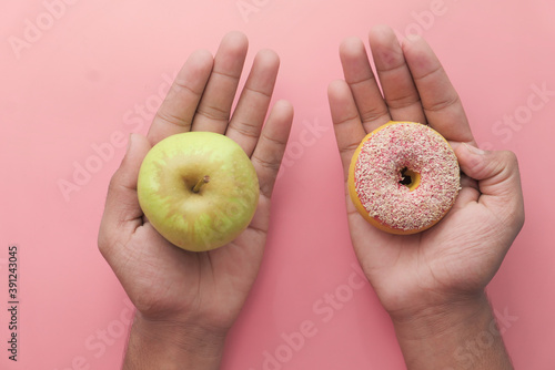 holding apple fruit and donut, choose healthy food concept.