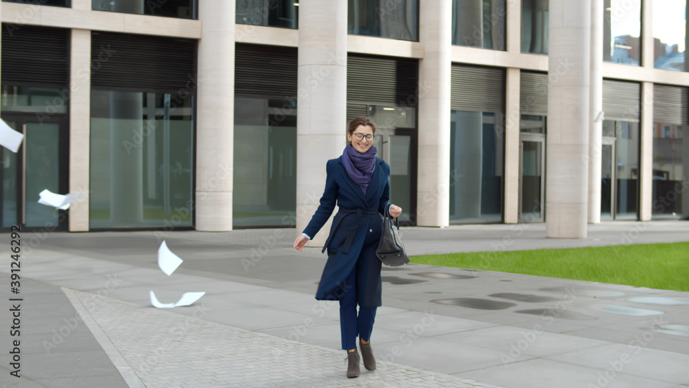 Excited businesswoman walking out business center throwing document away Excited businesswoman walking out business center throwing document away