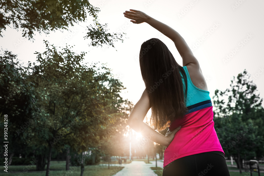 Young woman stretching before morning run in park, back view. Space for text