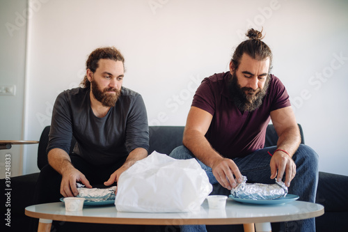 Two bearded friends open some dürums that they bring from a take away to lunch at home