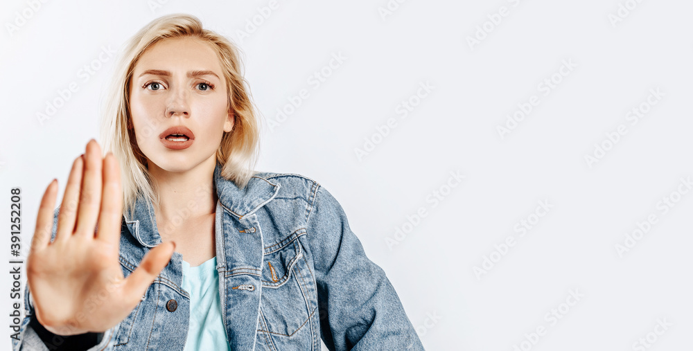 Beautiful young girl unhappy frown and says stop with a hand gesture on gray isolated background Beautiful young girl unhappy frown and says stop with a hand gesture on gray isolated background