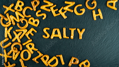Obraz na płótnie Salty text among bread sticks letters on black background. Salty crisps fonts. Unhealthy diet, junk snacks concept. w salonie