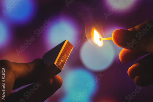 Man lits fire to a match while holding a matchbox in his hand on a beautiful background with bokeh