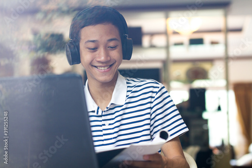 Candit of Asian boy having fun with online teacher by video call on laptop computer at home. smiling young man enjoying online course on application. photo