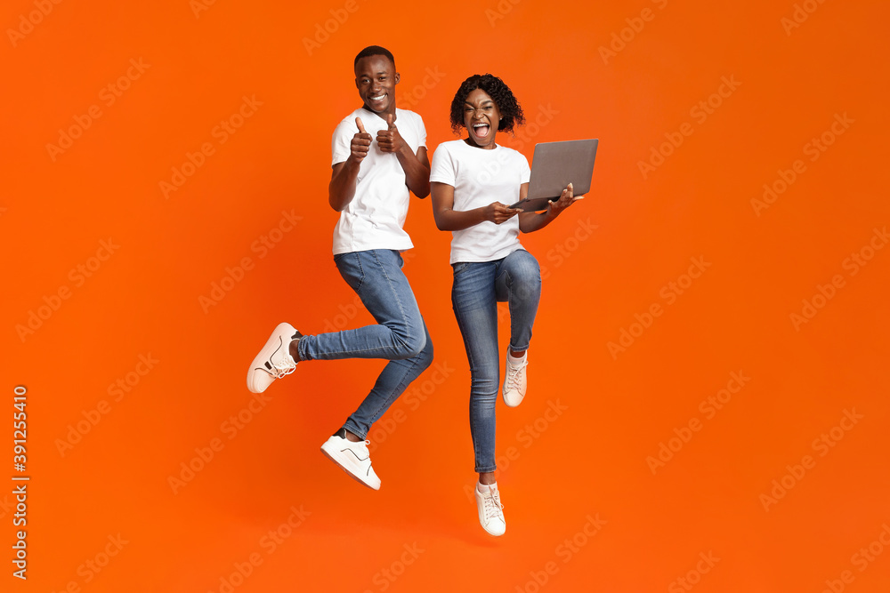 Excited black couple jumping up with laptop