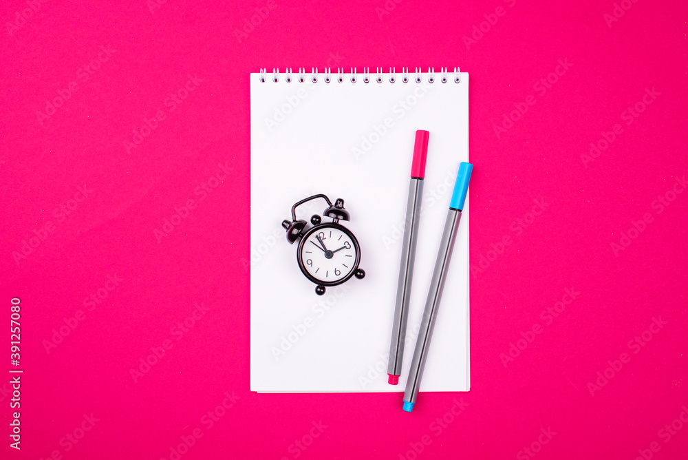 A white notebook for recordings, two handles of different colors a small black alarm clock on a red background. A white notebook for recordings, two handles of different colors a small black alarm clock on a red background.