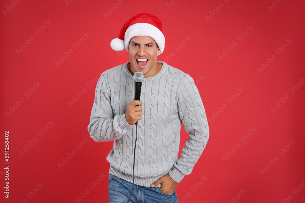 Happy man in Santa Claus hat singing with microphone on red background. Christmas music
