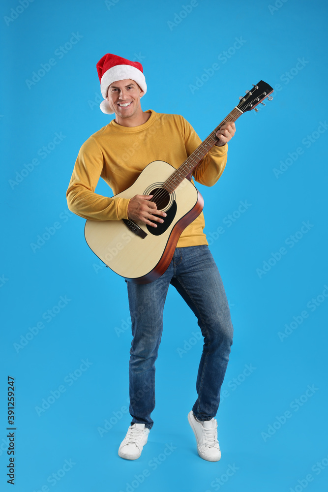 Man in Santa hat playing acoustic guitar on light blue background. Christmas music Man in Santa hat playing acoustic guitar on light blue background. Christmas music