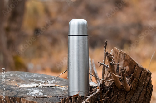 Outdoor vacuum steel thermos. Camping flask in the autumn forest. Hike concept, relaxation in nature, hot drink in cold weather.