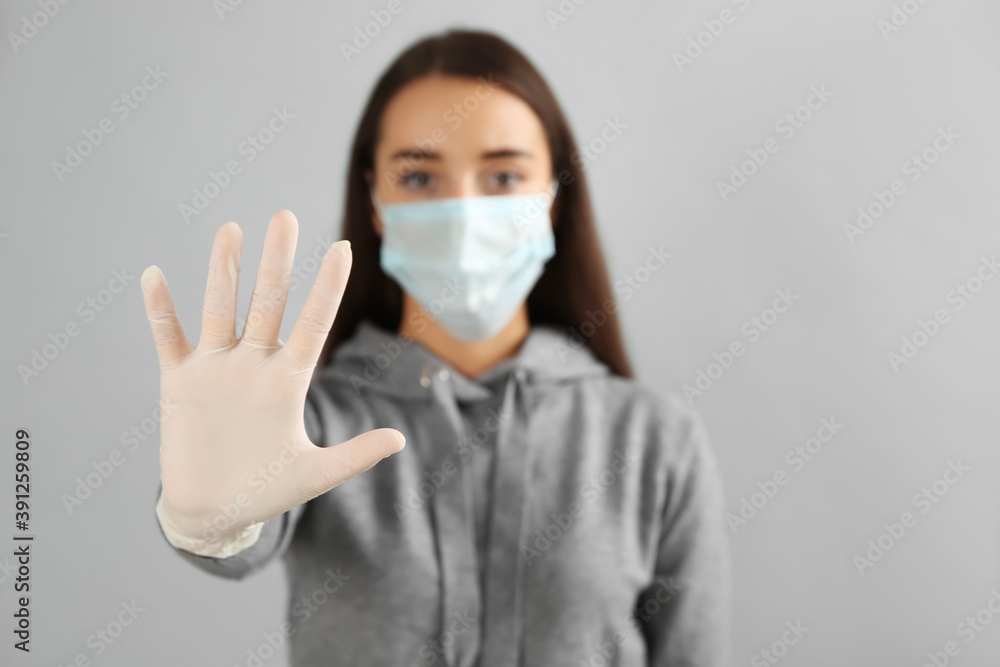 Woman in protective face mask and medical gloves showing stop gesture against grey background, focus on hand Woman in protective face mask and medical gloves showing stop gesture against grey background, focus on hand