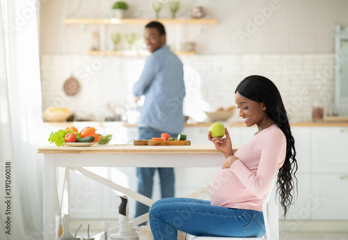 Beautiful pregnant woman with apple and her loving boyfriend cooking balanced meal at kitchen  copy space